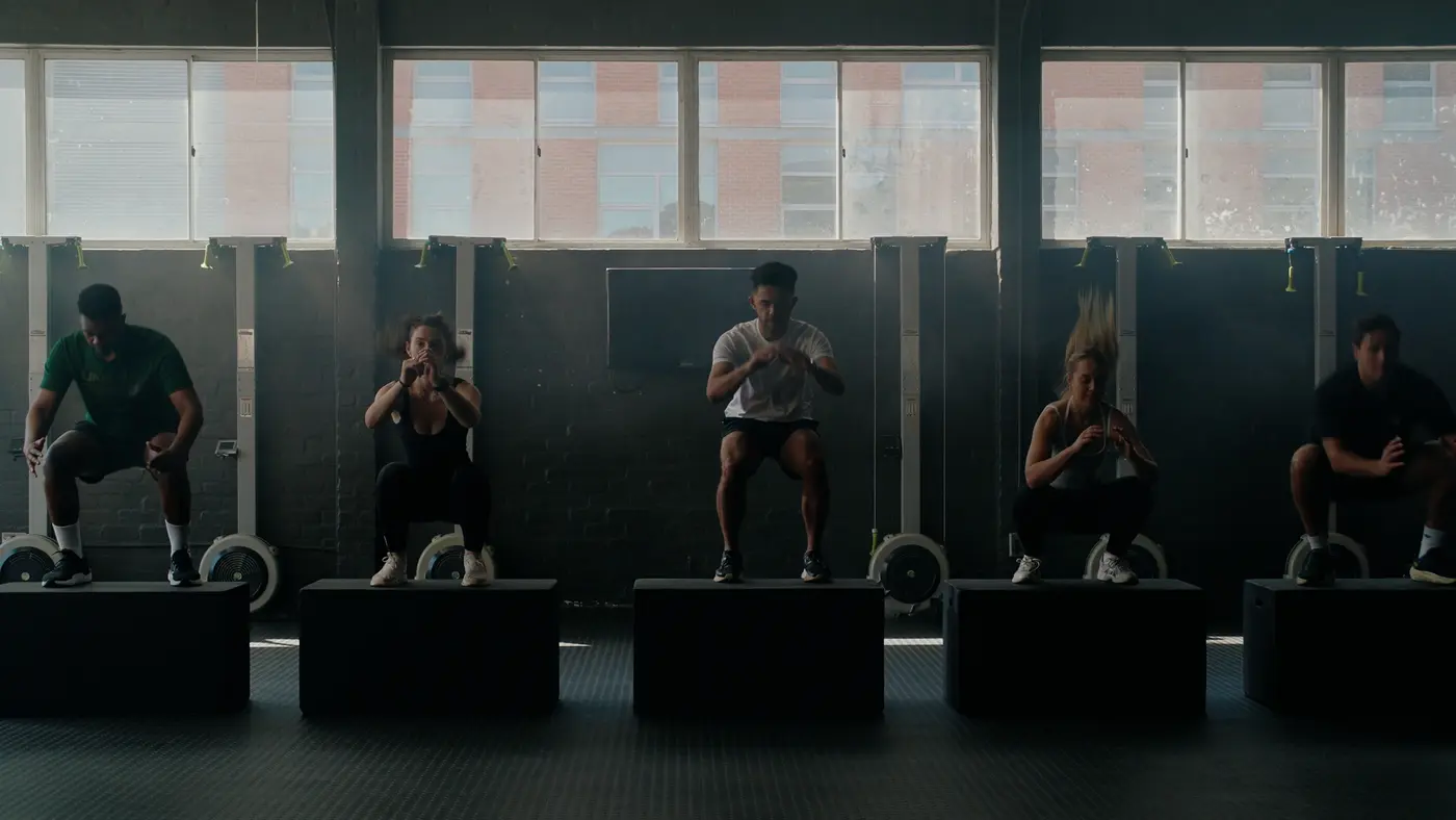 A class of five doing box jumps in a sunlit studio